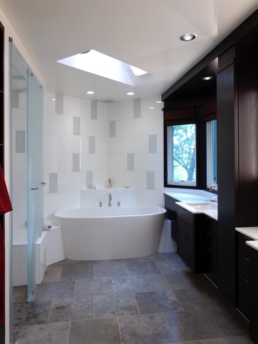 View of tub, vanities to right; shower on left. Materials are limestone floors, glass tile walls.